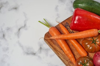 Ahşap mutfak masasında çeşitli sebzeler ve sebzeler beyaz mermer bir yüzey. Havuç, biber, kabak, domates ve soğan. Metin için boşluk ile.