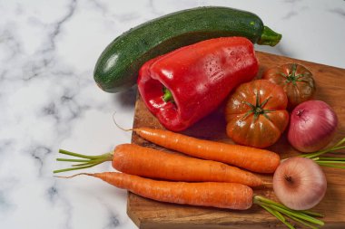 Ahşap mutfak masasında çeşitli sebzeler ve sebzeler beyaz mermer bir yüzey. Havuç, biber, kabak, domates ve soğan. Metin için boşluk ile.