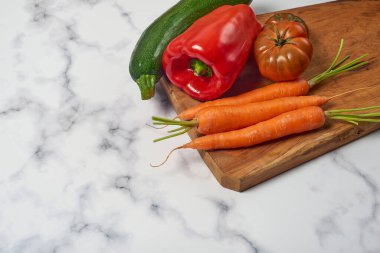 Ahşap mutfak masasında çeşitli sebzeler ve sebzeler beyaz mermer bir yüzey. Havuç, biber, kabak, domates ve soğan. Metin için boşluk ile.