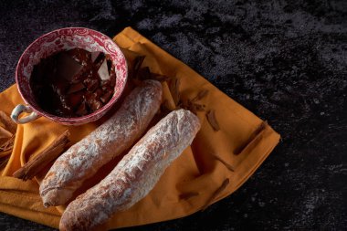 Osuruklar, İspanya, Valencia 'dan tipik hamur işleri, sıcak çikolatalı, Çin seramik kabında, sarı bir bezin üstünde, koyu bir yüzeyi var. Tatlı bir kahvaltı veya atıştırmalık..