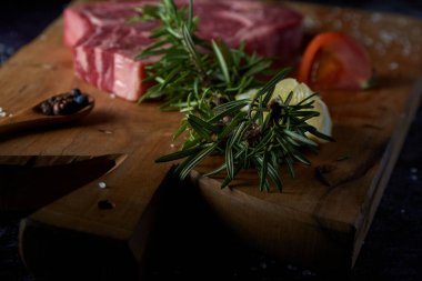 Tahta tahtada taze ve çiğ biftek, tuzlu ve koyu yüzeydeki diğer baharatlar. Biftek ızgaraya hazır. Kara yemek. Et, domates, biber, limon ve biberiye..