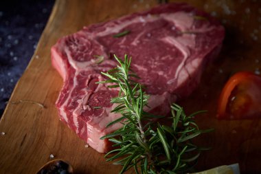 Tahta tahtada taze ve çiğ biftek, tuzlu ve koyu yüzeydeki diğer baharatlar. Biftek ızgaraya hazır. Kara yemek. Et, domates, biber, limon ve biberiye..