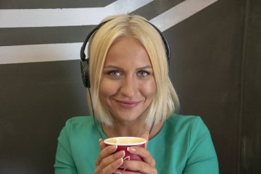 25-30 yaşlarında güzel bir sarışın bir bardak sıcak kahveyle kulaklık takıyor, müzik dinliyor ve eğleniyor..