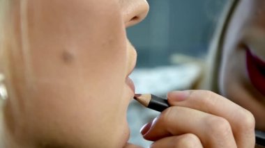 Makyaj ustası bir güzellik salonundaki müşterinin dudaklarına dokunuyor..