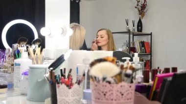 Kozmetik uzmanı kadın bir müşterinin dudaklarını boyuyor..