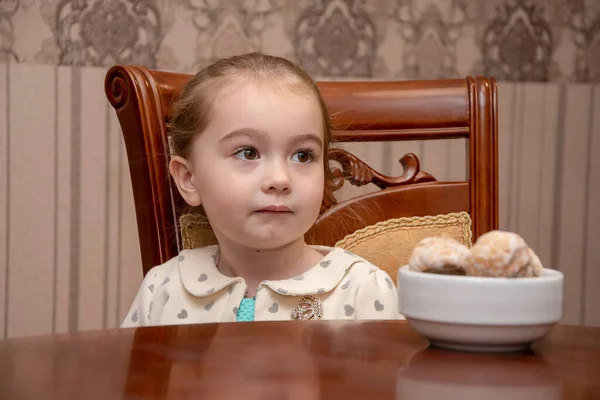一个小女孩坐在房间里的木桌边吃姜饼的画像 — 图库照片