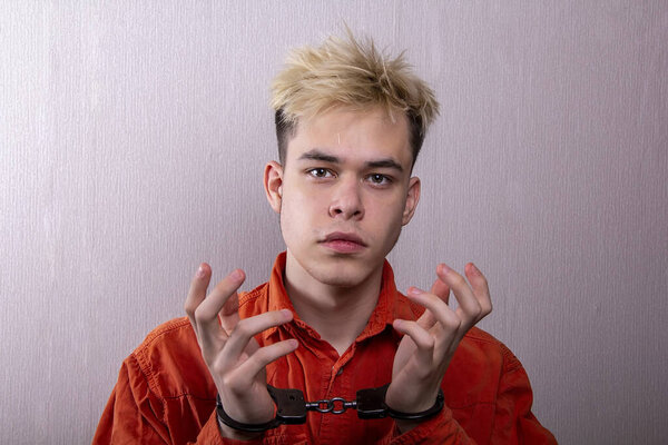 подросток в наручниках на сером фоне. несовершеннолетний преступник, уголовная ответственность несовершеннолетних. Члены молодежных преступных группировок и банд.