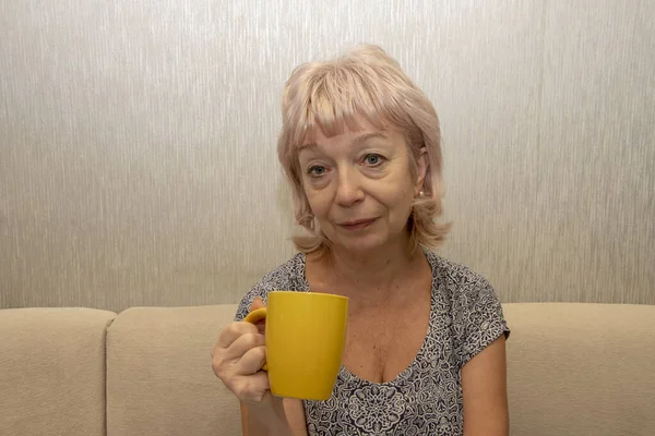一个没有化妆的60 65岁的女人的画像 她坐在家里的桌子旁 手里拿着杯子 节假日后的早上 退休年龄 — 图库照片