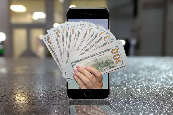 Bir kadının eli cep telefonundan gelen yüz dolarlık banknotları, bulanık bir şehir arkaplanını, yağmur damlalarını tutuyor. Konsept: mobil uygulama, banka kredisi veya piyango kazananı üzerinden para transfer etmek.