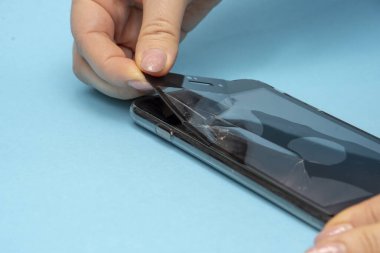 Kadınların elleri, akıllı telefonun kırık koruyucu camını soyar. Kavram: cam değiştirme, telefon tamiratı kendi ellerinle..