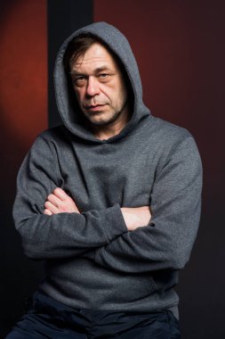 Studio portrait of a 40-50-year-old serious man in a gray hoodie on a neutral background with a hood on his head, looking at the camera, close-up. Maybe he's an actor or a retired military man.