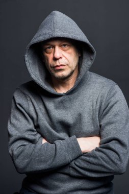 Studio portrait of a 40-50-year-old serious man in a gray hoodie on a neutral background, looking at the camera, eyes swollen. Maybe he's an actor or a truck driver, a lawyer or a retired military man.