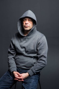 Studio portrait of a 40-50-year-old serious man in a gray hoodie on a neutral background, eyes directed at the camera, swollen eyes. Maybe he's an actor or a truck driver, a lawyer or a retired military man.