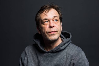 Studio portrait of a 40-50-year-old man in a gray hoodie on a neutral background, close-up, eyes directed to the side. Maybe he's an actor or a truck driver, a lawyer, or a retired military man.