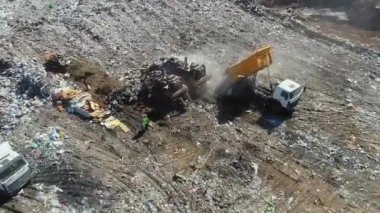 Açık şehir çöplüğünün manzarası, çöpleri boşaltan kamyonet, çöpleri gömen buldozerler, uçan martılar..