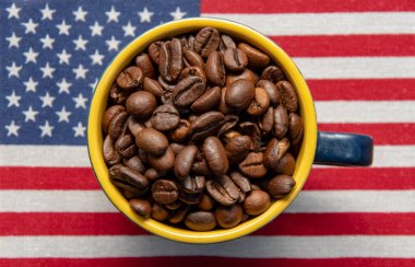 Amerikan bayrağında, ağzına kadar kızarmış kahve çekirdeği dolu bir kahve fincanı duruyor. Kavram: Amerikan kahvesi, zengin tat, ihracat ve Amerika 'dan ithalat.