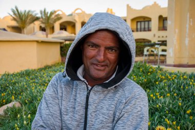 40 yıllık gülümseyen esmer tenli bir adamın portresi güzel binaların arka planında, yakın plan. Belki de cankurtaran ya da turist rehberi olarak çalışıyordur..