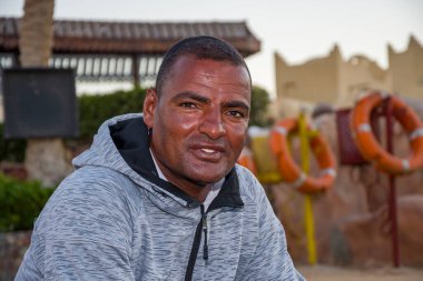 Açık bir turist plajında 40 yıllık esmer tenli bir adamın portresi can simidinin arka planında, yakın plan. Belki de turistler için cankurtaran ya da rehber olarak çalışıyordur..