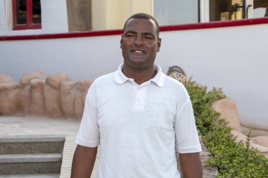 40 yıllık gülümseyen esmer tenli bir adamın portresi güzel binaların arka planında, yakın plan. Belki de cankurtaran ya da turist rehberi olarak çalışıyordur..