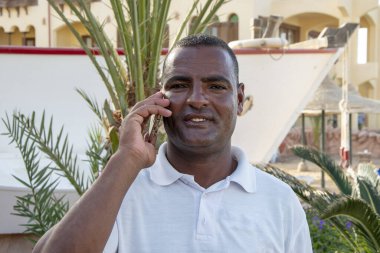 Telefonda konuşan siyahi adam palmiye ağaçları ve şehir manzarası hakkında konuşuyor..