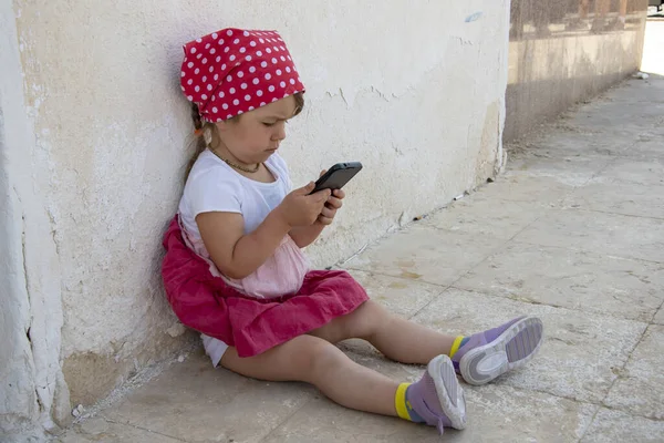 Mała Dziewczynka Siedząca Ulicy Patrząca Telefon Komórkowy Opierająca Się Ścianę — Zdjęcie stockowe
