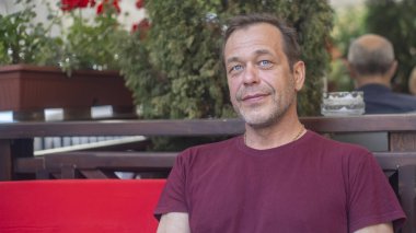45-50 yaşlarındaki gülümseyen bir adamın sokak portresi açık bir yaz kafesinde, dinlenme ve turizmde..