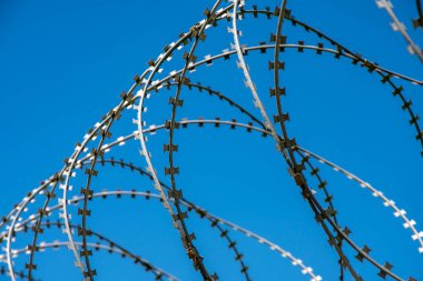 Mavi gökyüzüne karşı askeri dikenli teller. Kavram: Demir Perde, işgal rejimi, giriş ve çıkış yasağı, özgürlük kısıtlaması.