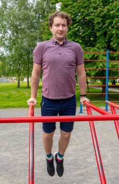 30-35 yaşlarındaki bir adam yazın açık hava spor sitesinde düzensiz barlarda şınav çeker. Kavram: sağlıklı yaşam tarzı, fiziksel aktivite.