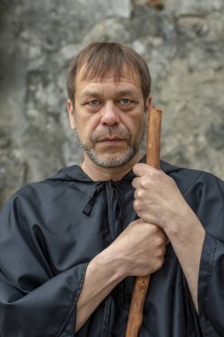 45-50 yaşlarındaki yaşlı bir keşişin portresi. Siyah cüppeli, sakallı ve arka planda asası olan bir rahip. Doğrudan kameraya bakıyor. Kavram: Şifa ve hac.