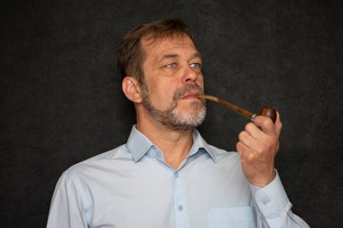 45-50 yaşlarında, yaşlı, güçlü bir adamın portresi gri sakallı, açık renk gömlekli ve siyah arka planda sigara piposu olan. Belki de bir aktör ya da emekli, yazar ya da sanatçıdır.