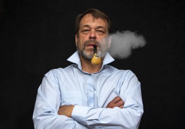 45-50 yaşlarında, yaşlı, güçlü bir adamın portresi gri sakallı, açık renk gömlekli ve siyah arka planda sigara piposu olan. Belki de bir aktör ya da emekli, yazar ya da sanatçıdır.