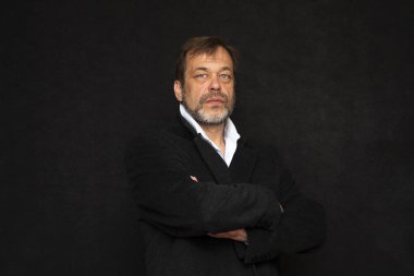 45-50 yaşlarında, siyah takım elbiseli, gri sakallı ve koyu renk gömlekli yaşlı ve şık bir adamın portresi. Belki de bir aktör ya da eski bir müzisyen ya da emekli askerdir.