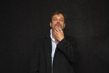 45-50 yaşlarında, siyah ceketli, açık renk gömlekli, sakalını kaşıyan ya da okşayan yaşlı bir adamın portresi..