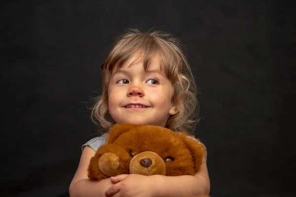 一个鼻子刮伤的小女孩在黑暗的背景下抱着一只泰迪熊 — 图库照片