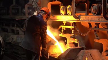 Bir çelik işçisi, çelik endüstrisindeki kalıplara erimiş metal döker. Taşıyıcı hareket eder..
