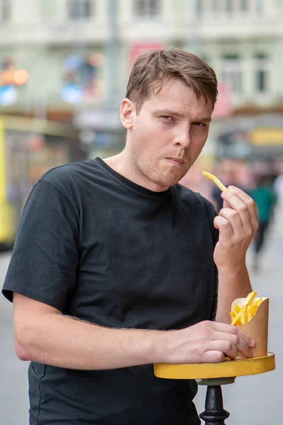 一个年轻人在一个模糊的城市景观的背景下吃薯条的街头肖像 城市里的快餐 街头食品 — 图库照片