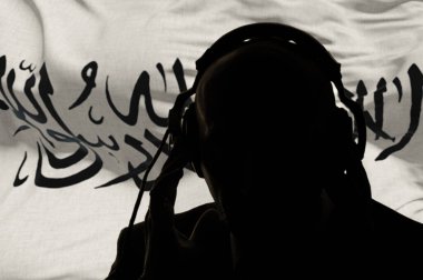 Taliban bayrağının arka planında kulaklık takan bir adamın silueti, gizlice dinleyen bir gizli ajan, casus ve istihbarat subayı, İslamcı beyaz bir bayrak,.