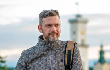 35-40 yaşlarında, sırtında sırt çantasıyla gülümseyen bir adamın portresi. Eski mimari yapıların bulanık arka planına karşı. Konsept: Turizm ve seyahat, ikamet değişikliği.