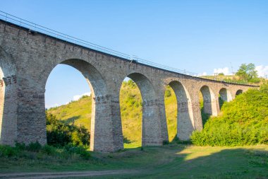 Dağlarda viyadük. Tepeler arasındaki taş demiryolu köprüsü doğanın arka planında, akşam aydınlatması.