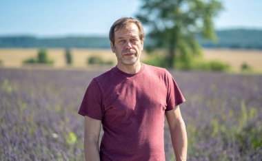 45-50 yaşlarında lavanta tarlasının arka planında tişört giyen bir adamın portresi. Konsept: emeklilikte seyahat, yaşlılar için aromaterapi.