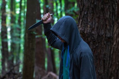 Bir adam ormanın yukarısından büyük bir bıçakla bıçaklıyor, yakın plan, seçici odaklanma. Konsept: Yoldan geçenlere saldırı, bir tecavüzcü ve bir katil, orman kuşağındaki bir suç, bir suçlu ve bir korku.