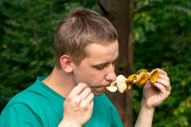 Bir adam ormanda bir çubuğa bağlanmış çiğ mantar yiyor. Konsept: çiğ gıda, mantar zehirlenmesi, ormanda hayatta kalma.