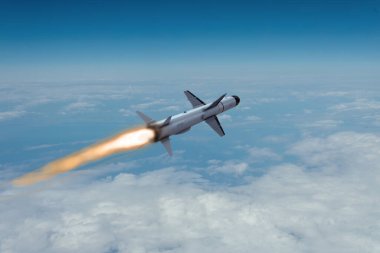 Modern bir anti-gemi seyir füzesi bulutların arasında yüksek irtifada uçar ve mavi gökyüzünde parlak bir alev izi bırakır.