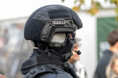 Bir polis, insanlar arasında koruyucu bir miğfer ve maske takıyor.