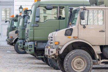 Askeri kamyonlar, parlak idari binanın yanındaki kaldırım taşlarının üzerinde yan yana dizildi. Avusturya, Viyana, 26 Ekim 2025