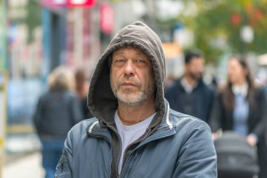 50-55 yaşlarında, başlık takmış yaşlı bir Avrupalı, yoldan geçen insanların arasında bir şehir caddesinde.