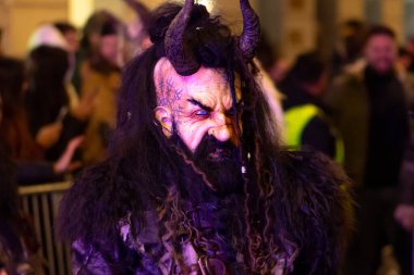 Siyah boynuzlu ve maskeli bir karakter sokakta yürüyor.