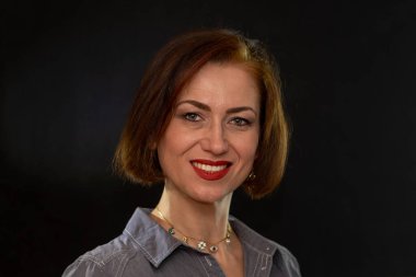 Stüdyonun arka planında düzgün saç stili ve makyajlı gülümseyen orta yaşlı bir kadının portresi.