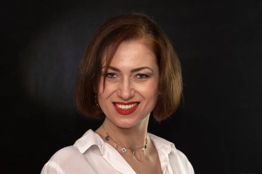 Gülümseyen orta yaşlı, düzgün saç stili ve etkileyici makyajlı bir kadının stüdyo portresi.
