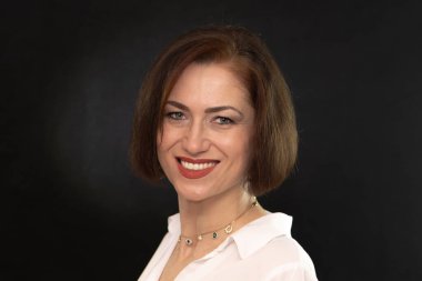 Bir kadın karanlık bir arkaplanda poz verir, sakin ve kendinden emin bir görüntü yaratır.